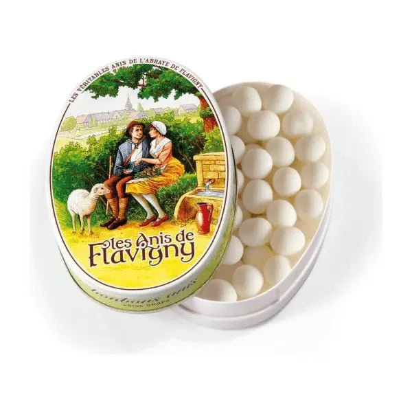 An oval tin of Twice as Sweet Anis De Flavigny Anis 50g (France), partially open to show small white aniseed candies. The lid displays vintage art of a couple sitting outdoors with a sheep nearby.