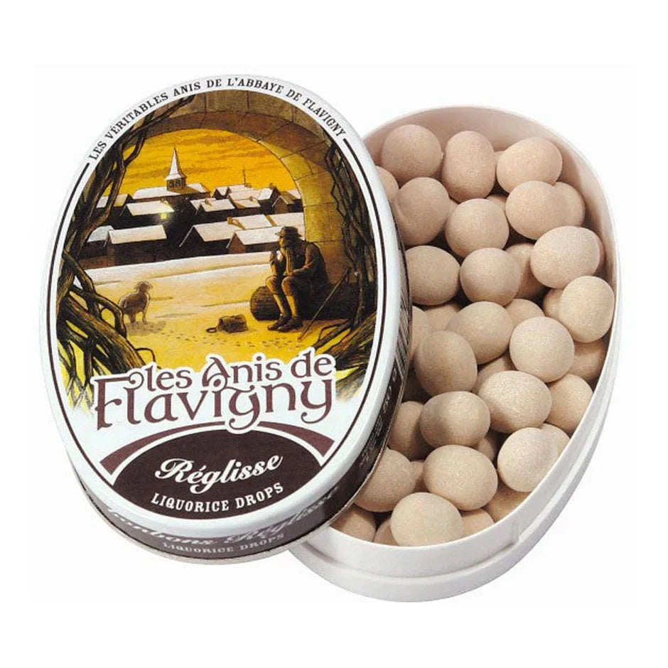 An open 50g tin of Twice as Sweet Anis De Flavigny Liquorice candy from France, featuring an abbey and countryside illustration on the lid and revealing classic round liquorice pastilles inside.