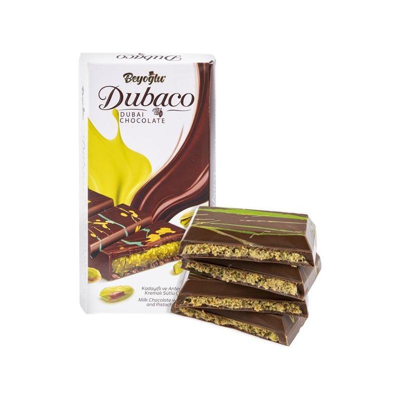 A box of Twice as Sweet Beyoglu Dubaco Dubai Pistachio Chocolate (Turkey) sits beside three stacked bars with layers of milk chocolate and pistachio—a Turkish treat whose packaging highlights both chocolate and pistachios.