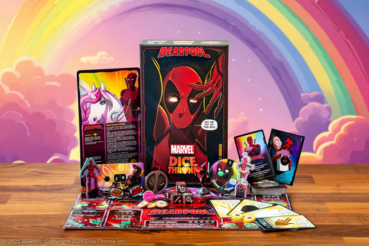 Deadpool Dice Throw board game set displayed on a wooden table with its box, cards, dice, and accessories arranged in front. The background features a colorful pastel rainbow and clouds.