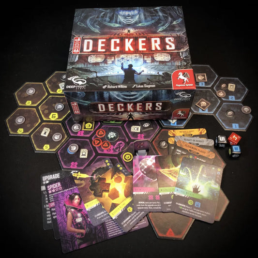 The board game Deckers shown with its box, hexagonal player tiles, cards, and dice on a black background.