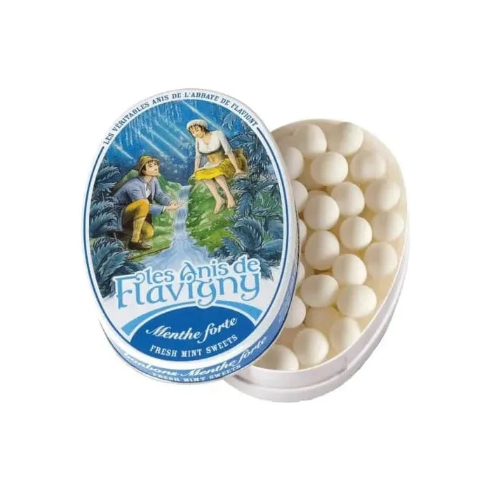 Partially opened oval tin of Twice as Sweet Anis De Flavigny Mint 50g (France), showing round white French candies. The lid displays vintage artwork of a man and woman in a blue, nature-inspired setting.