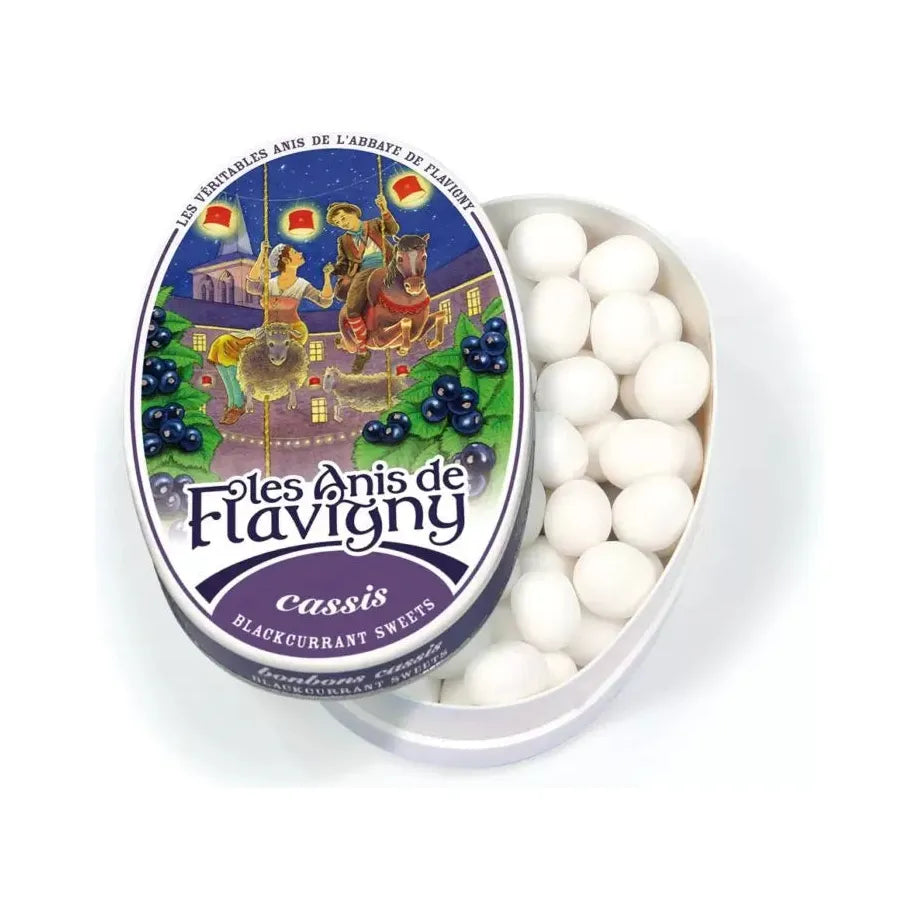 Partially open oval tin of Twice as Sweet Anis De Flavigny Blackcurrant candy (50g, France) reveals round white candies. The lid features a medieval-style illustration of a man and woman on a carousel horse.