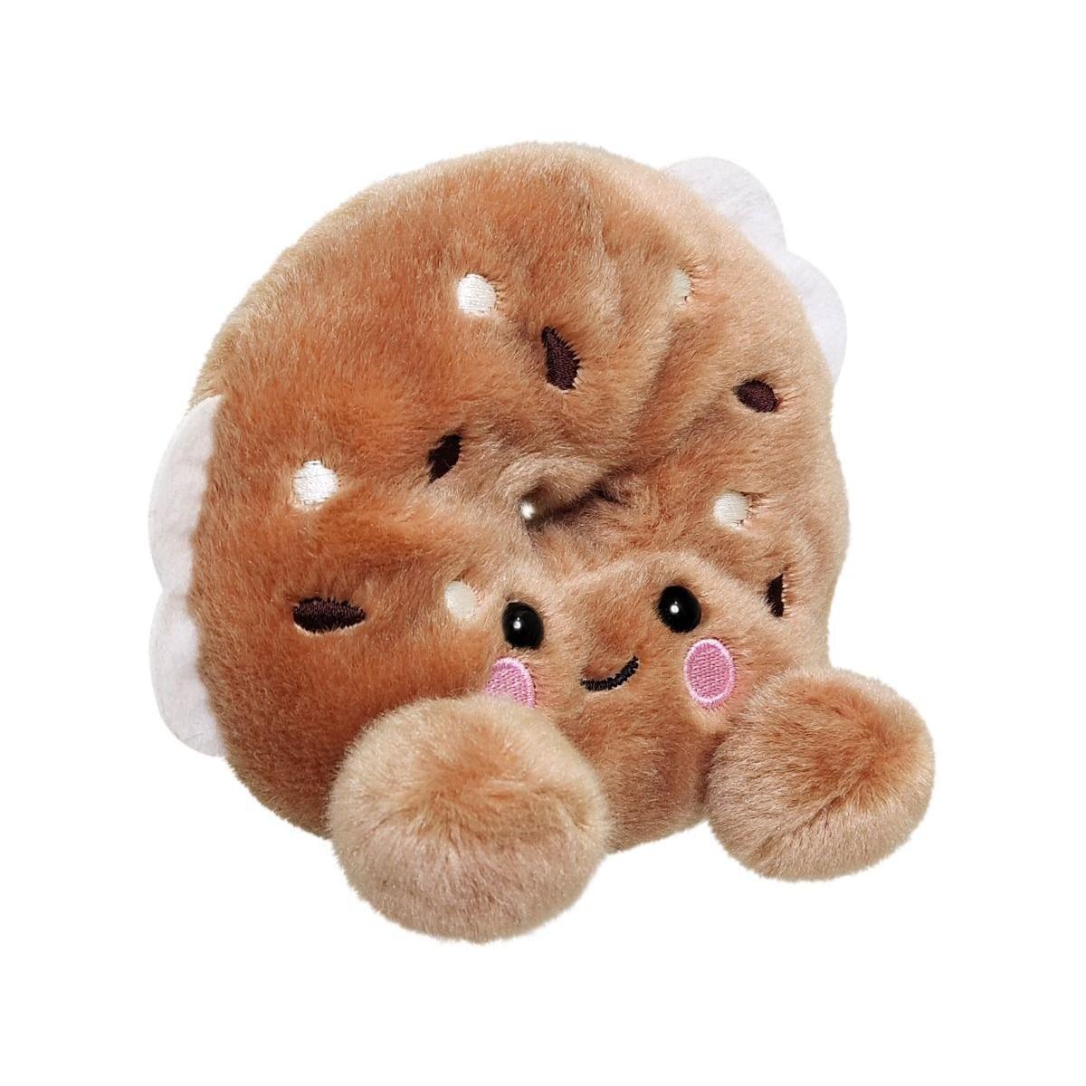 Palm Pal Tony Everything Bagel by Twice as Sweet is a plush toy shaped like a smiling bagel with embroidered eyes, pink cheeks, and two fluffy feet—an adorable collectible displayed against a white background.
