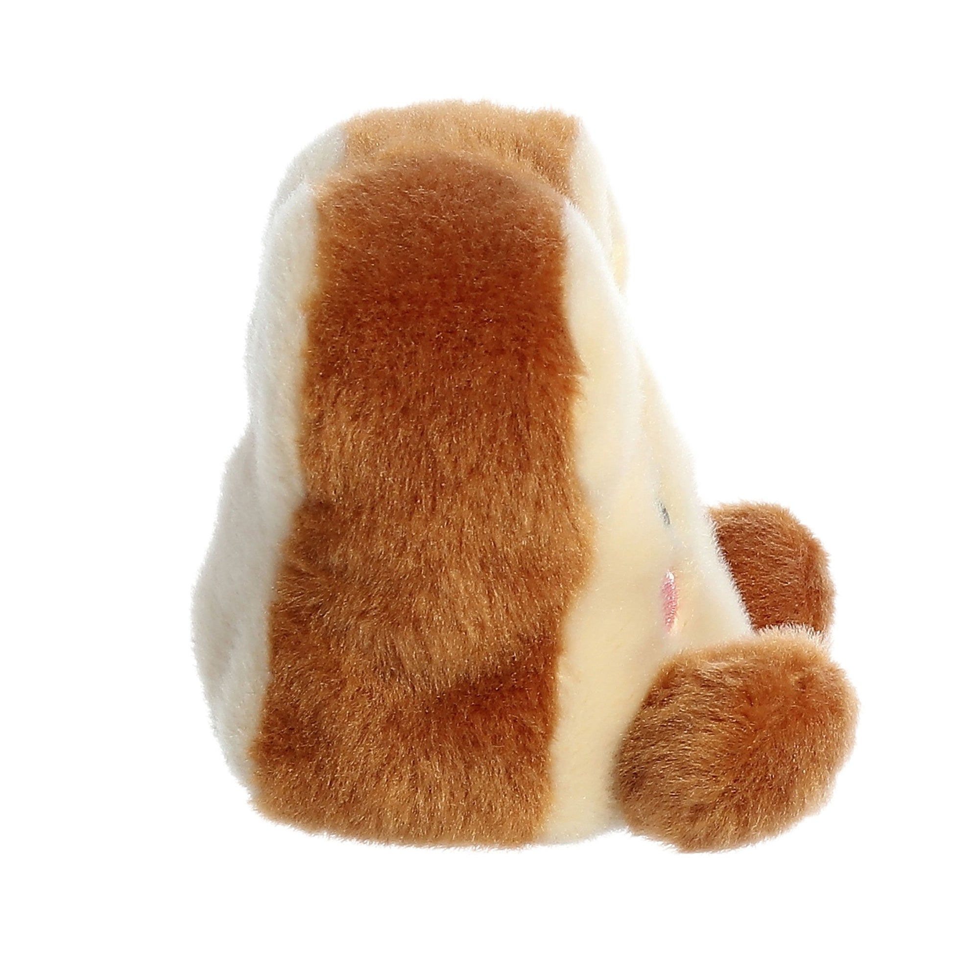 A side view of Palm Pal Buttery Toast by Twice as Sweet, a palm-sized plush with brown and cream fur, round body, two short legs, pink cheeks, and soft fuzzy texture—perfect as a breakfast-themed cuddle companion.