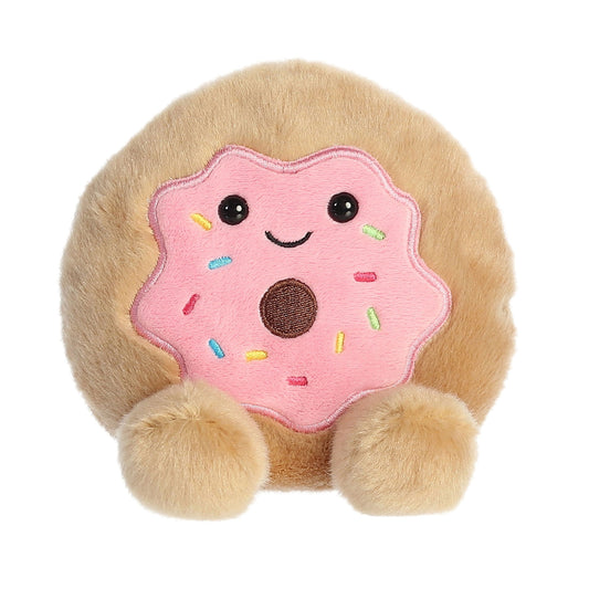 The Twice as Sweet Palm Pal Claire Donut is a plush toy with tan dough, a pink frosted top with colorful sprinkles, a smiling face, and two round fluffy feet.