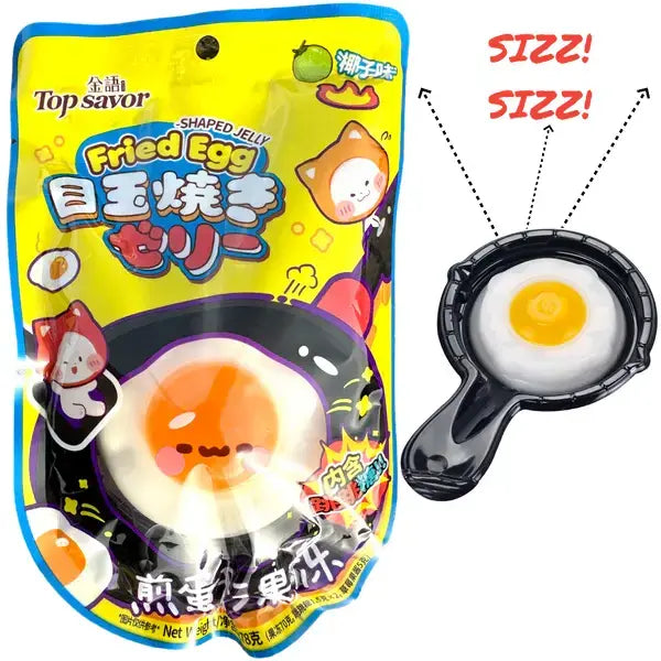 A colorful package of Twice as Sweet Fried Egg Jelly with Popping Candy 78g (Japan) shows a cartoon egg and cat. Beside it, a realistic fried egg jelly with popping candy sits in a small black skillet marked SIZZ! SIZZ!.