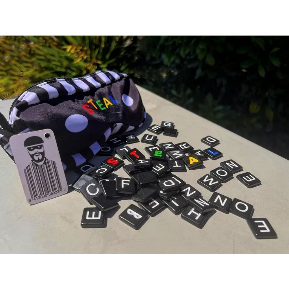 Steal board game contents with black letter tiles with colorful letters, a striped pouch, and a card on a light surface with a blurred green background.