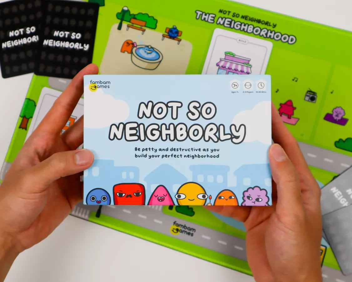 A person holds the front of the 'Not So Neighborly' board game box, showing the light blue packaging with cartoon characters. The green game board and other game pieces are visible in the background.