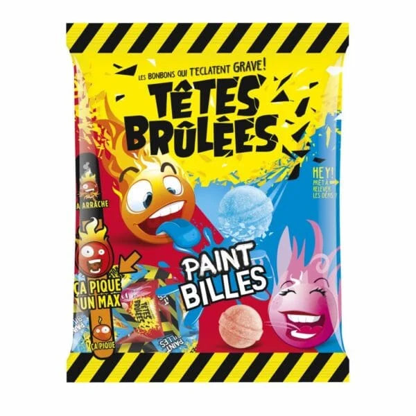 A vibrant bag of Twice as Sweet Têtes Brûlées Paint Billes 135g (France) features cartoon faces, black-and-yellow caution stripes, and French text. The colorful sour candy is shown in bold blue and red.