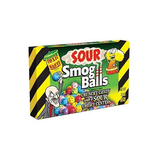 The image shows a 99g Toxic Waste Sour Smog Balls Theatre Box from Twice as Sweet, featuring yellow and green packaging with black stripes, cartoon characters, colorful sour candy balls, and the words “Crunchy Candy with a Sour Chewy Center” and “Toxic Waste.”.
