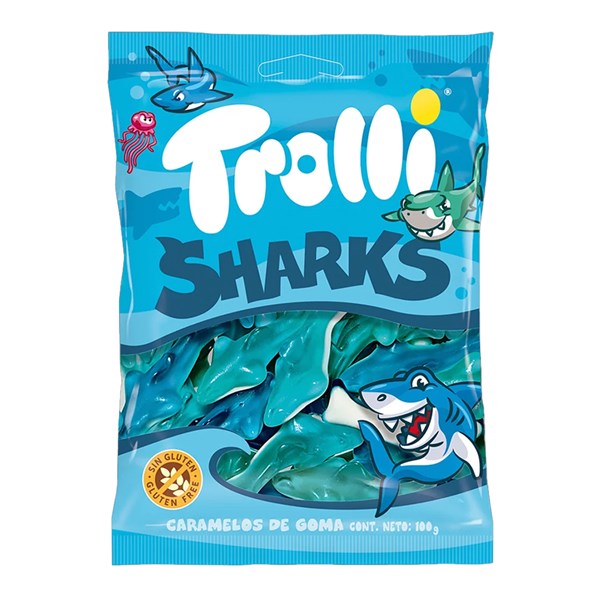 A 100g bag of Twice as Sweet Trolli Sharks (Spain) features blue and white shark-shaped gummies in blue packaging with cartoon sharks and a jellyfish, highlighting their fruity flavour and “Trolli Sharks” branding.